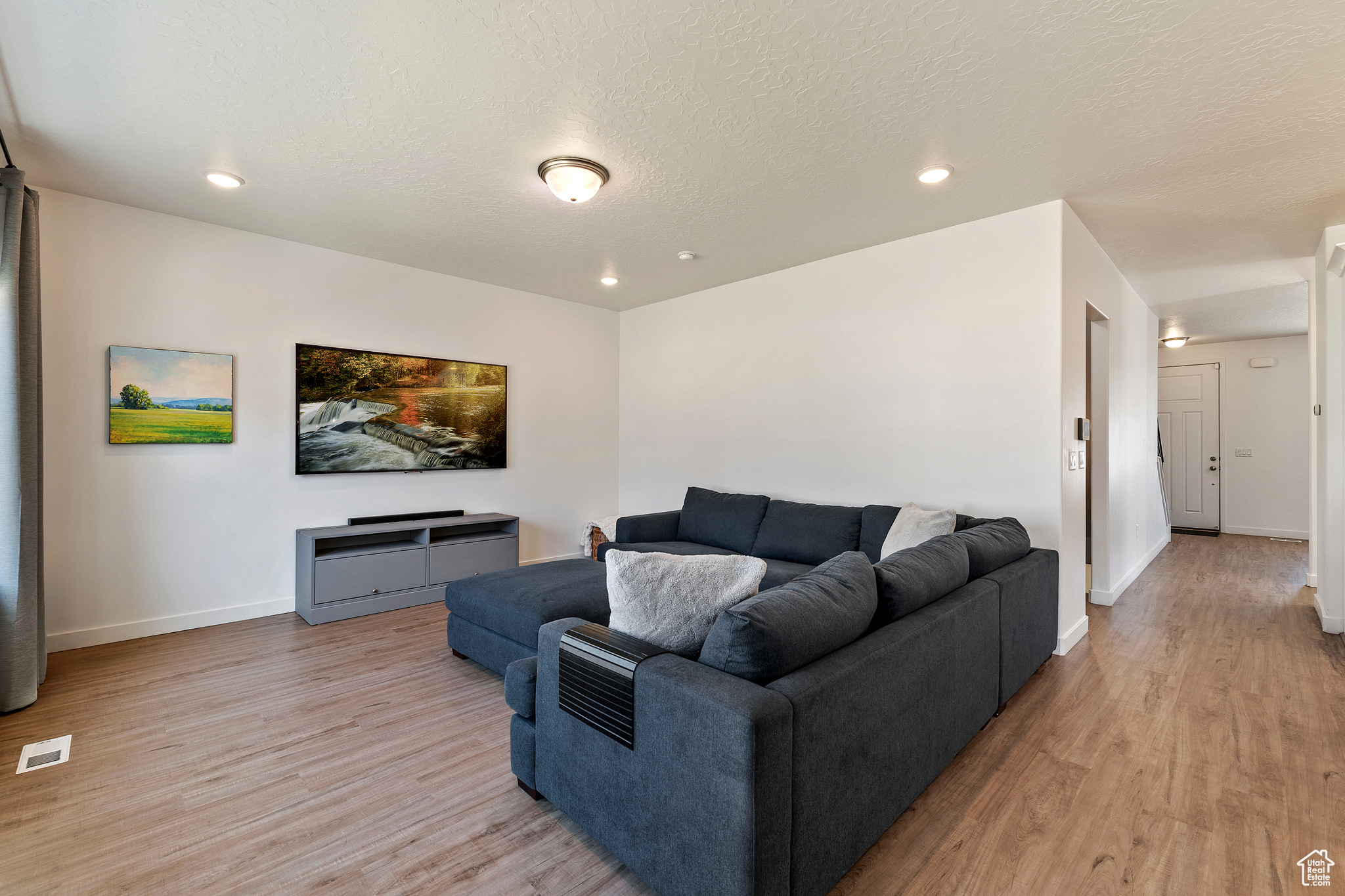 Living area featuring baseboards, visible vents, a textured ceiling, and light wood-style floors