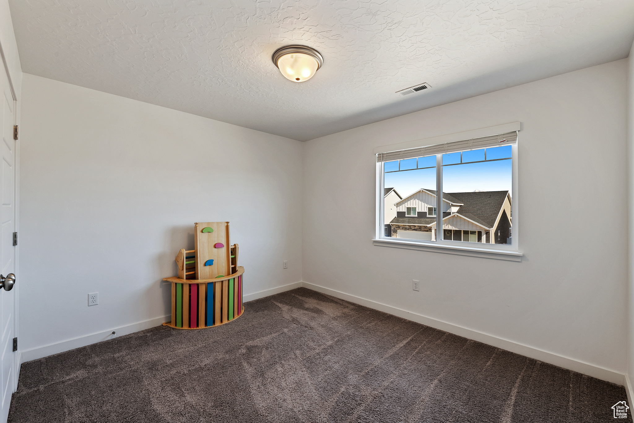 Carpeted spare room with visible vents, a textured ceiling, and baseboards