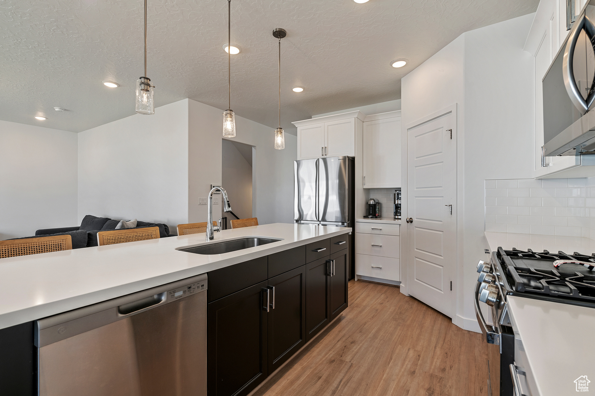 Kitchen with a sink, stainless steel appliances, light wood-style floors, white cabinets, and light countertops