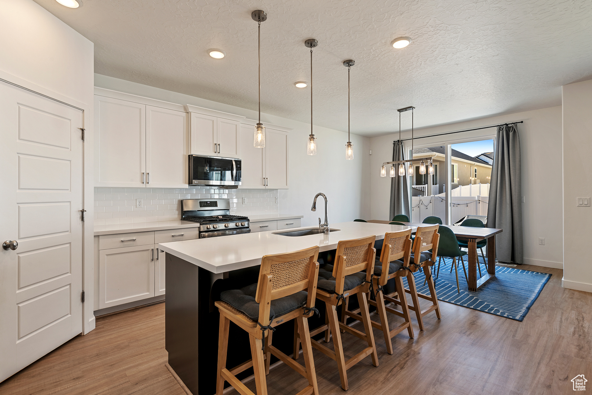 Kitchen with an island with sink, a sink, decorative backsplash, stainless steel appliances, and light wood-style floors