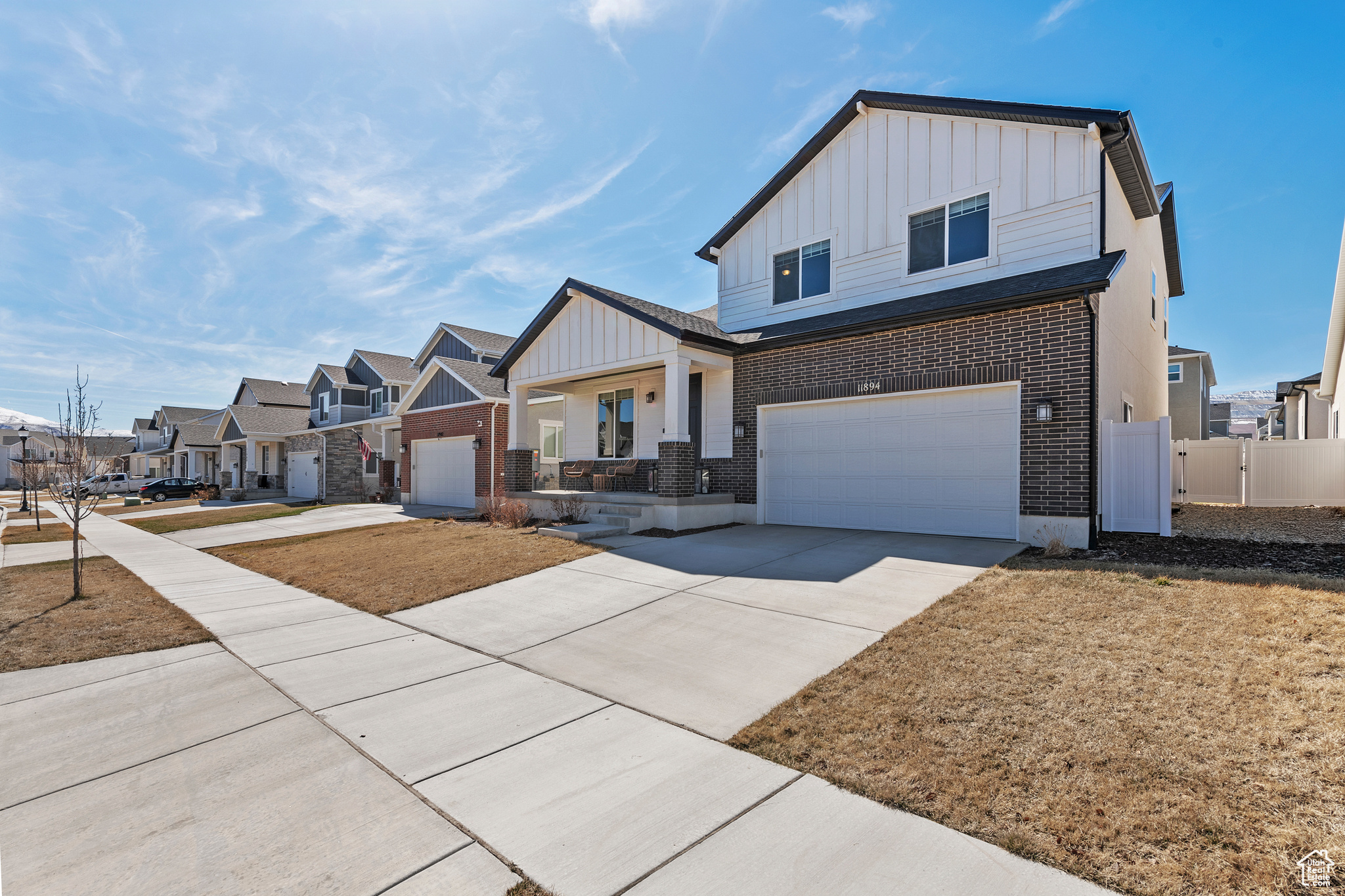 View of front of property featuring fence, a residential view, concrete driveway, board and batten siding, and brick siding