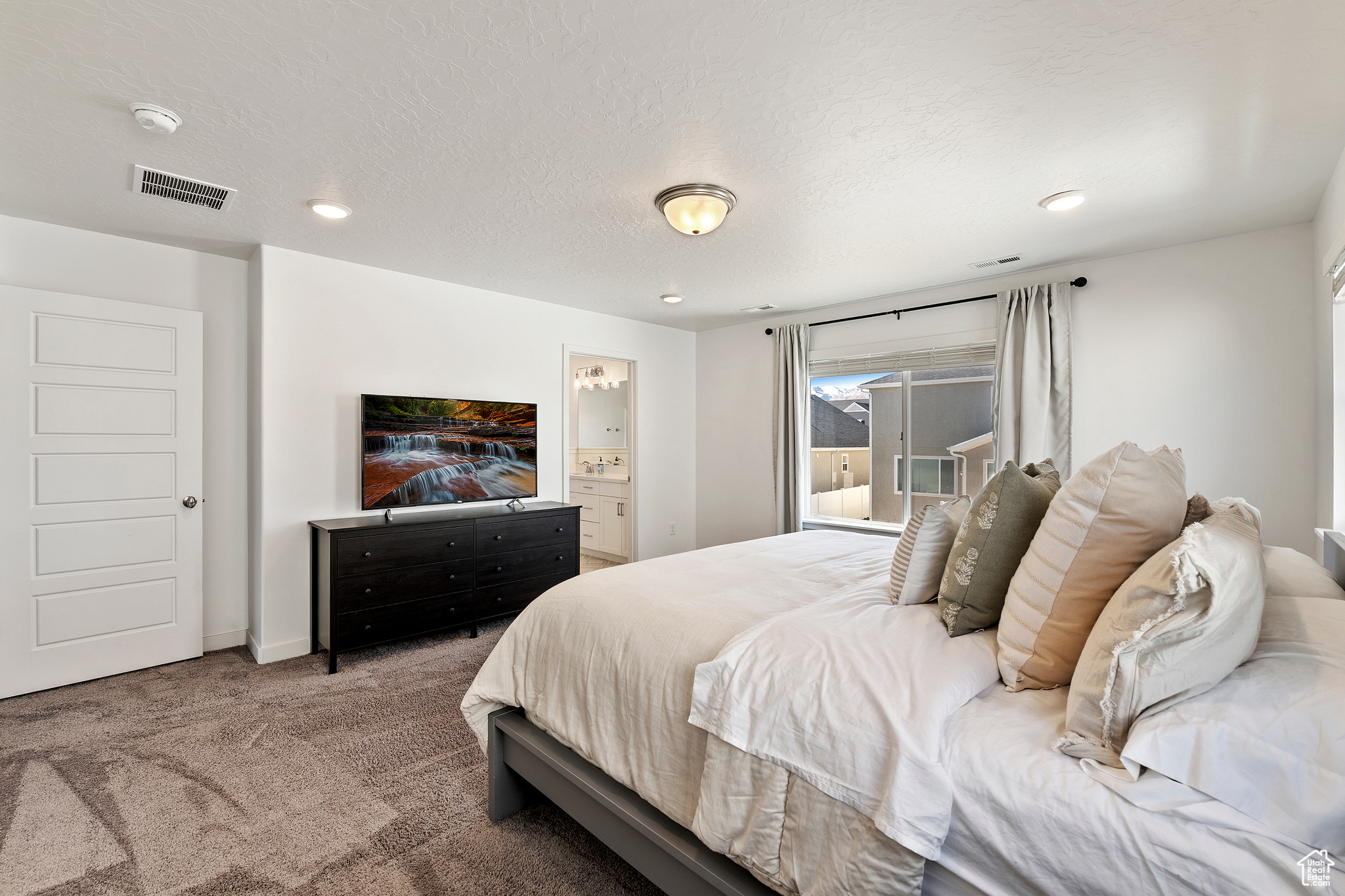 Carpeted bedroom featuring connected bathroom, recessed lighting, visible vents, and a textured ceiling