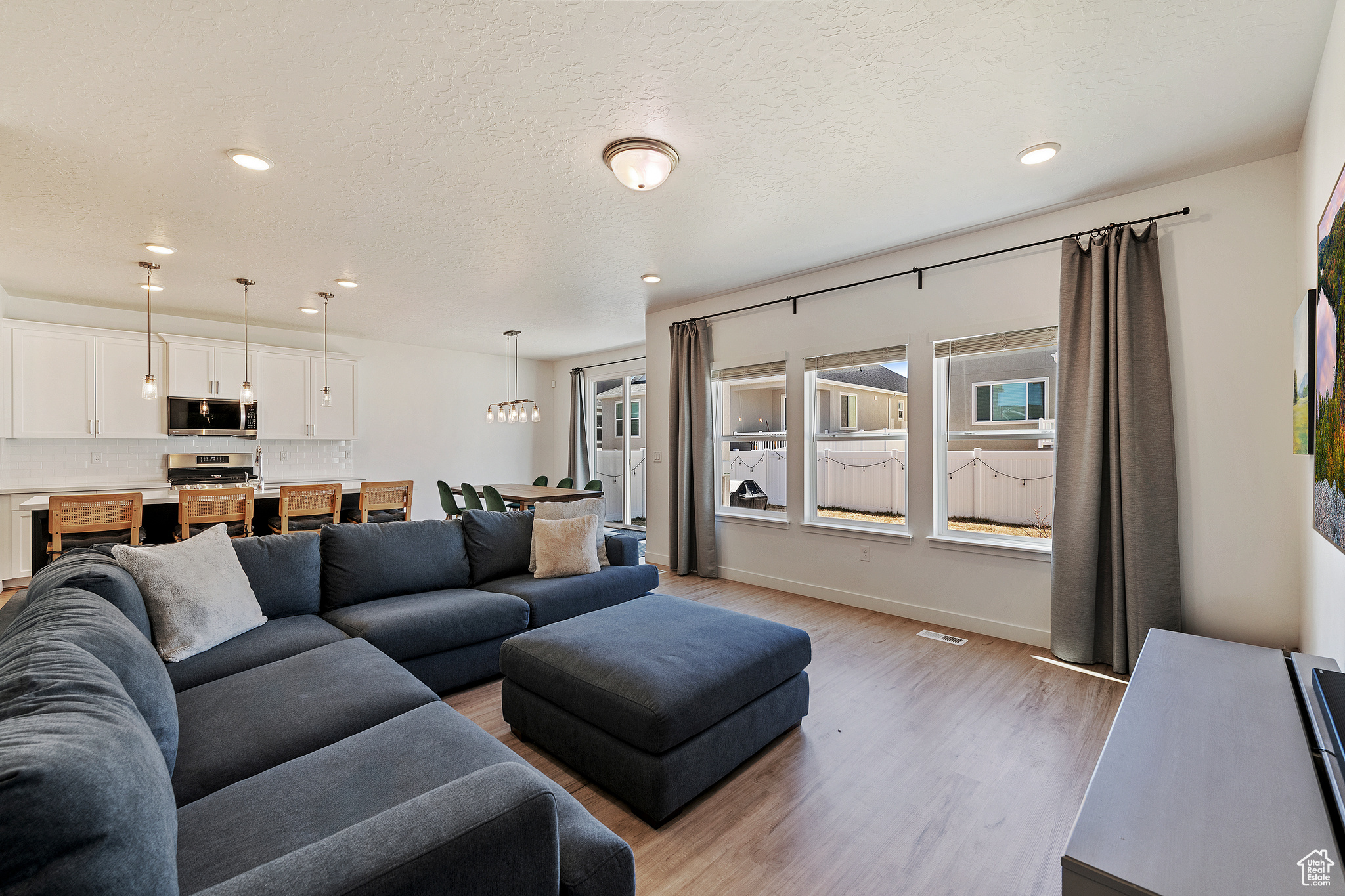 Living room with a textured ceiling, light wood-style floors, and a healthy amount of sunlight