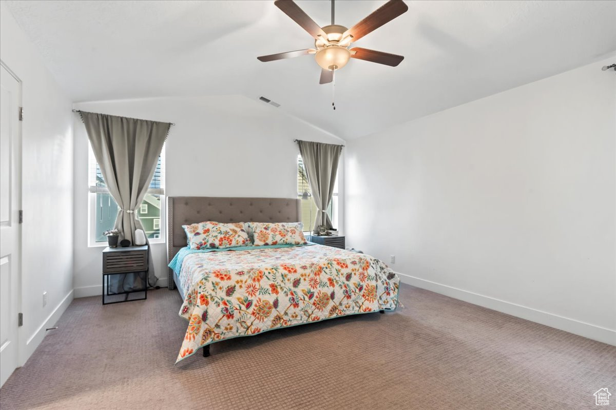 Carpeted bedroom featuring visible vents, vaulted ceiling, baseboards, and ceiling fan