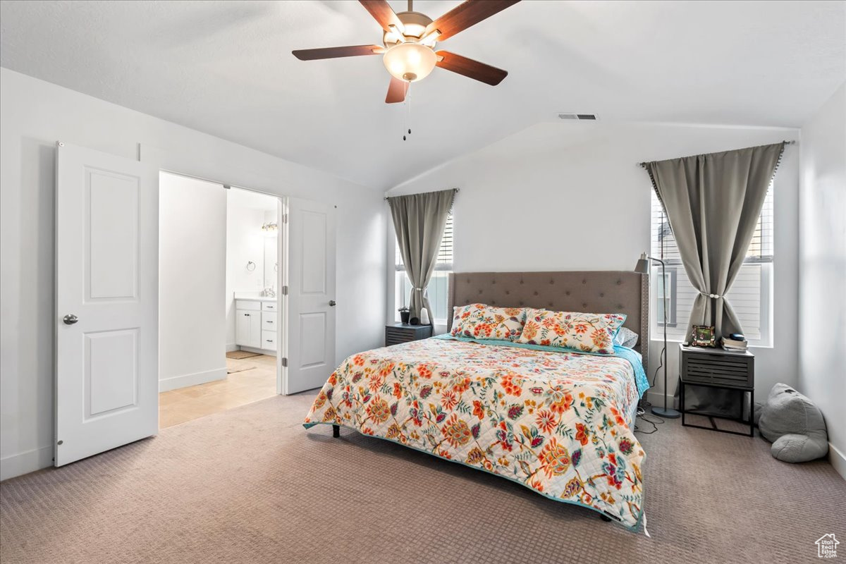 Carpeted bedroom featuring lofted ceiling, visible vents, connected bathroom, ceiling fan, and baseboards
