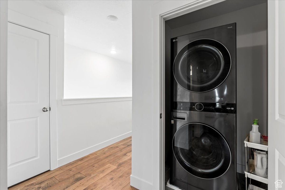 Laundry room with laundry area, stacked washer / dryer, wood finished floors, and baseboards