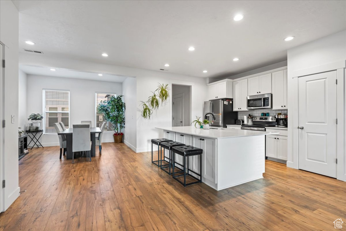 Kitchen with hardwood / wood-style flooring, stainless steel appliances, visible vents, a kitchen breakfast bar, and a center island with sink