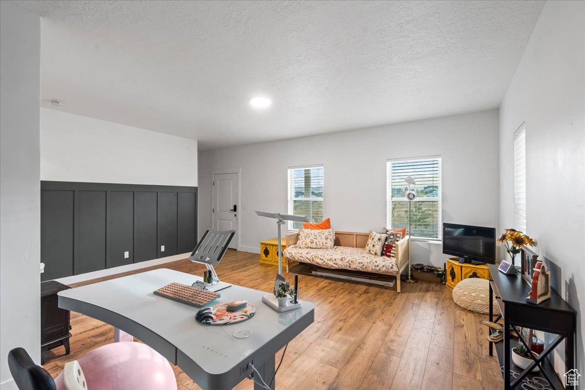 Living area with light wood-type flooring, a textured ceiling, and wainscoting