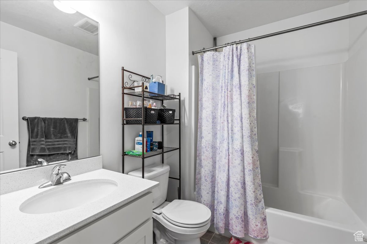 Full bathroom featuring shower / tub combo with curtain, visible vents, toilet, vanity, and tile patterned flooring