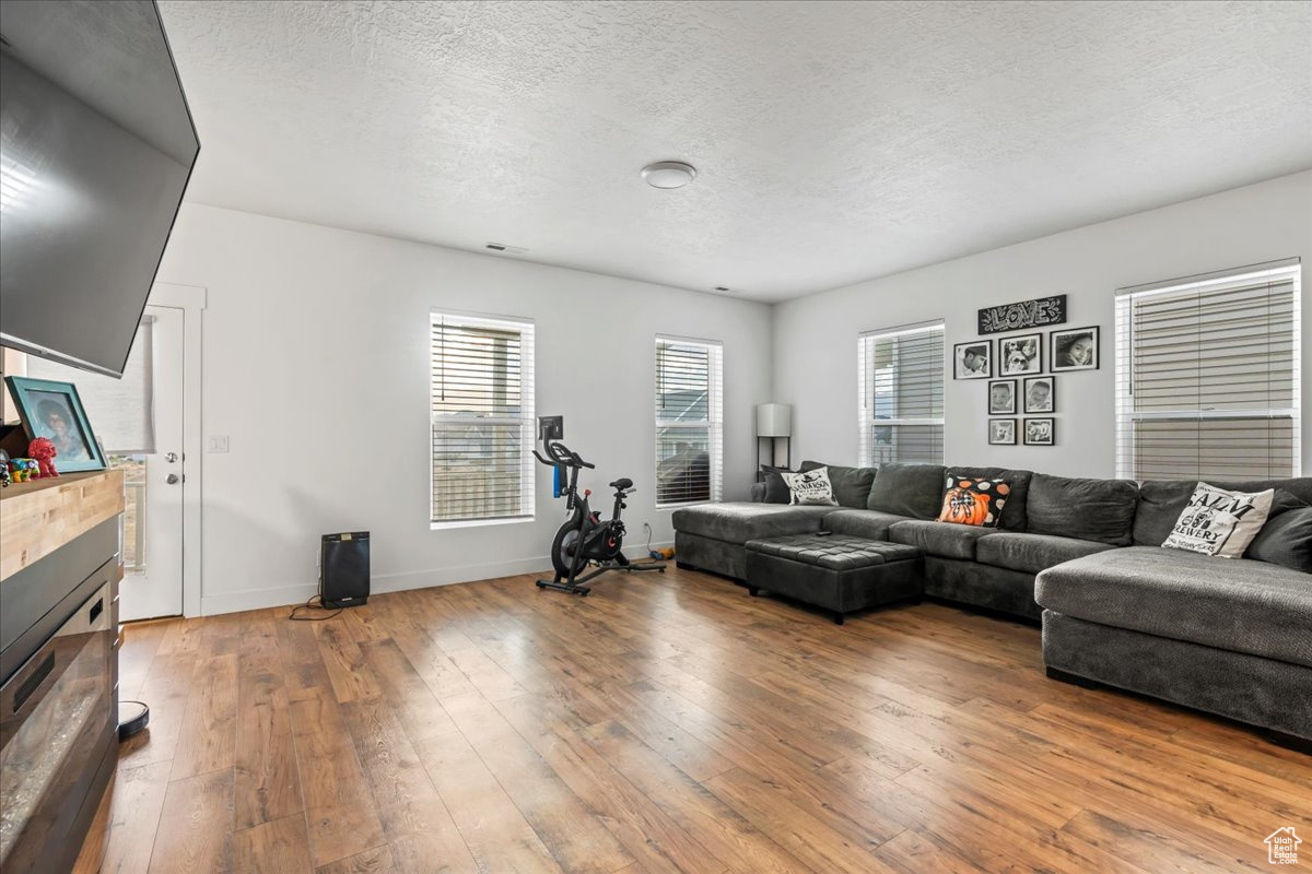 Living area with a textured ceiling, visible vents, baseboards, hardwood / wood-style floors, and a glass covered fireplace