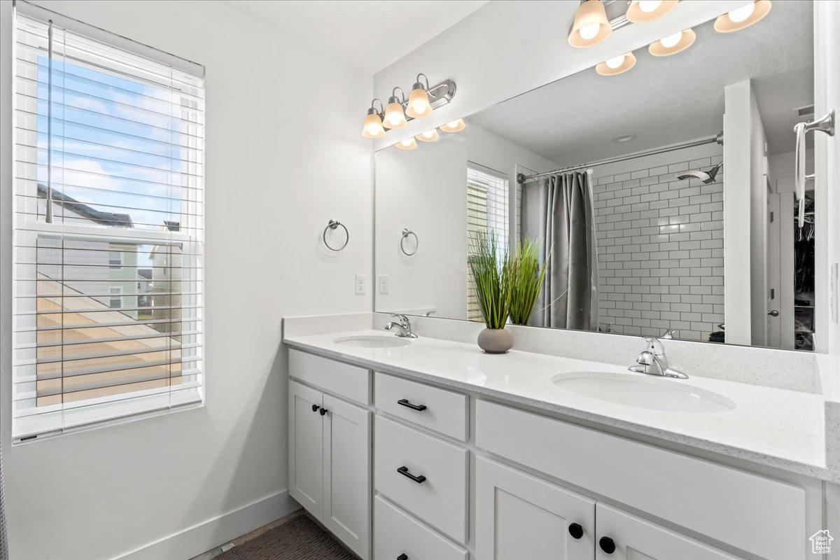 Full bath featuring double vanity, tiled shower, a sink, and baseboards