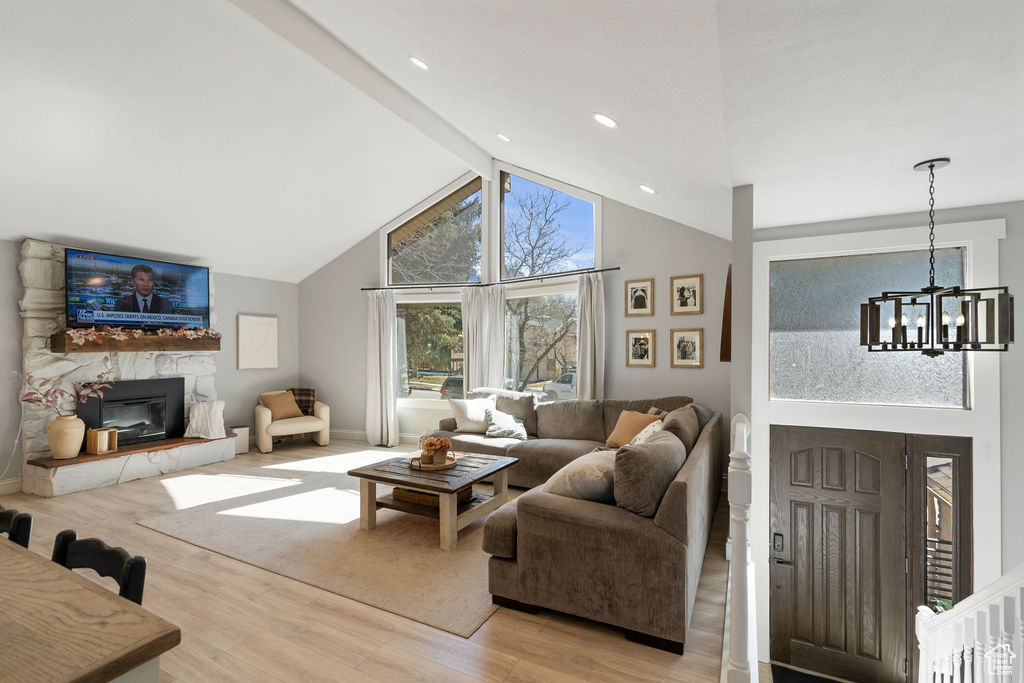 Living room featuring beam ceiling, high vaulted ceiling, a fireplace, light wood finished floors, and a chandelier