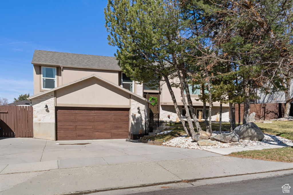 View of front facade featuring stucco siding, driveway, fence, a shingled roof, and a garage