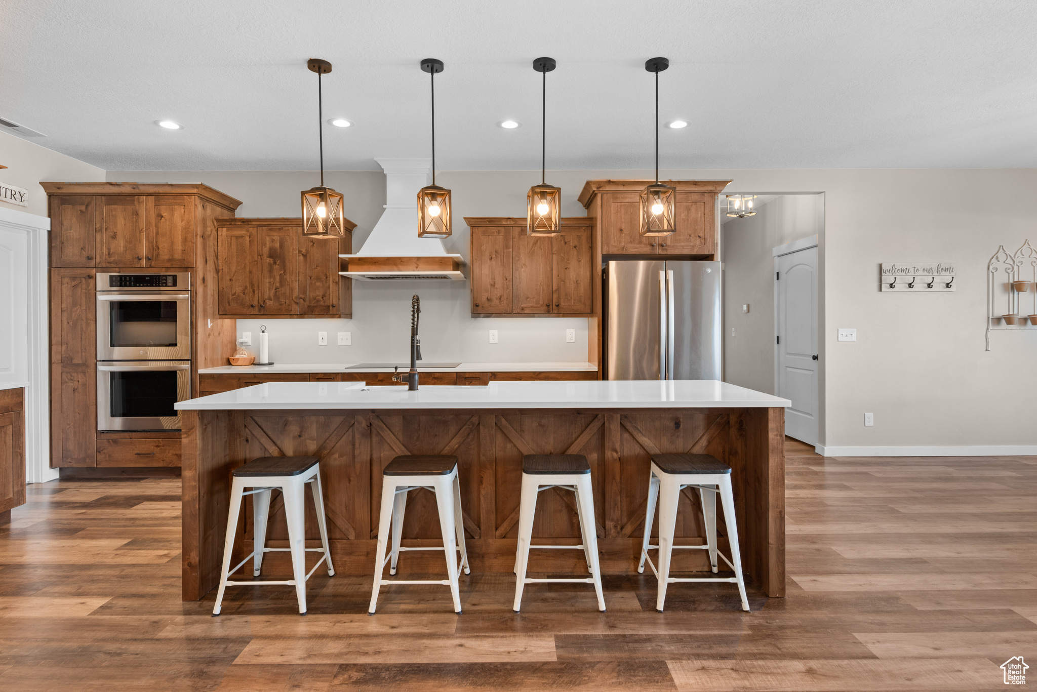 Kitchen featuring premium range hood, appliances with stainless steel finishes, brown cabinetry, and wood finished floors