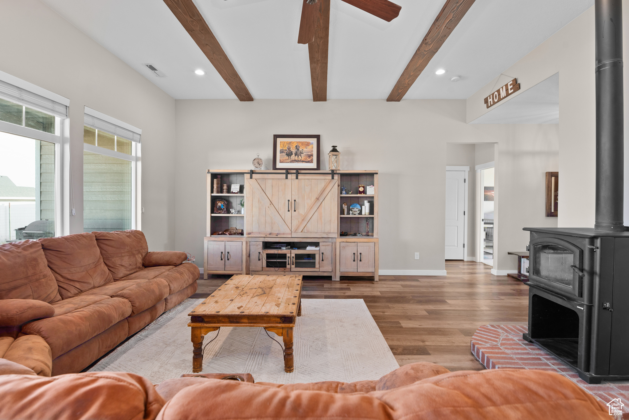 Living room with visible vents, beamed ceiling, wood finished floors, and a wood stove