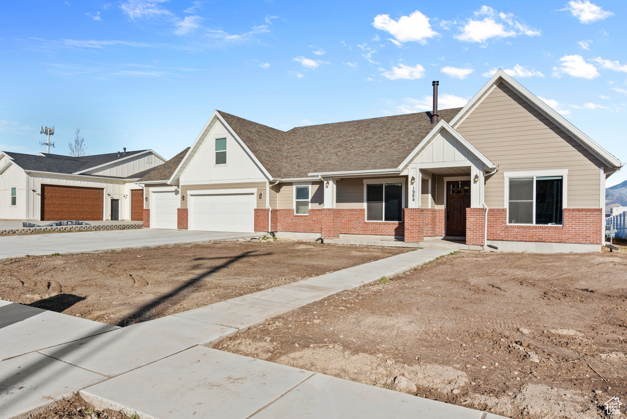 View of front of property with board and batten siding, concrete driveway, brick siding, and roof with shingles