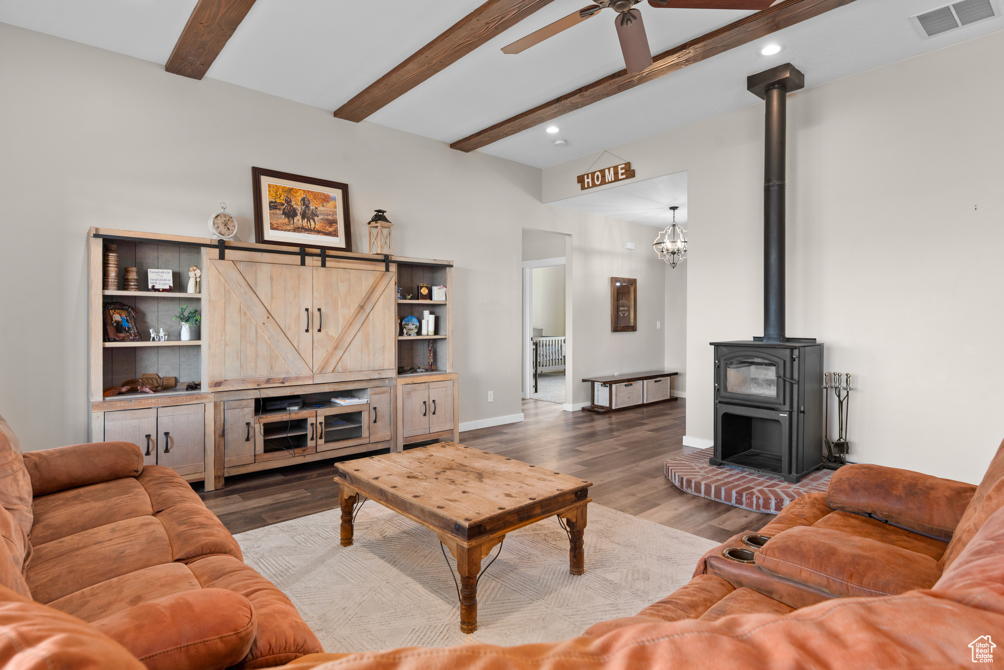 Living room with visible vents, a ceiling fan, wood finished floors, a wood stove, and beam ceiling