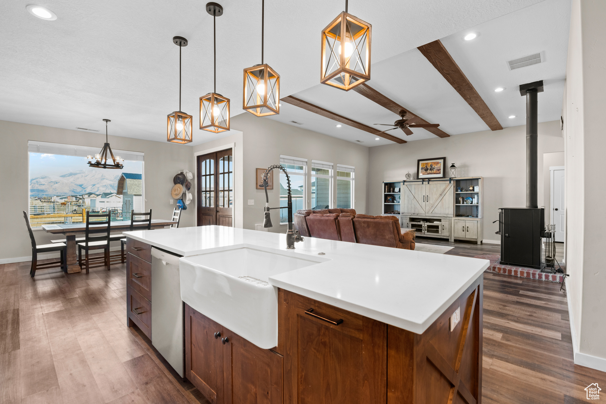 Kitchen featuring beam ceiling, dark wood-style flooring, light countertops, stainless steel dishwasher, and a sink