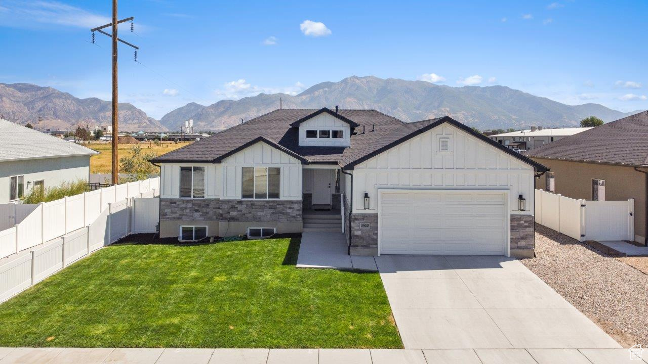 View of front facade featuring board and batten siding, an attached garage, a front yard, driveway, and a mountain view