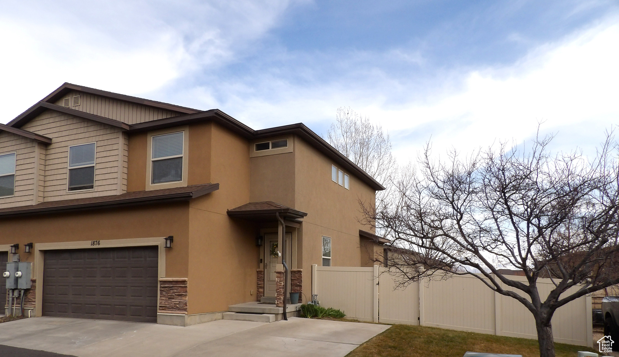 View of front facade featuring stone siding, stucco siding, driveway, and fence