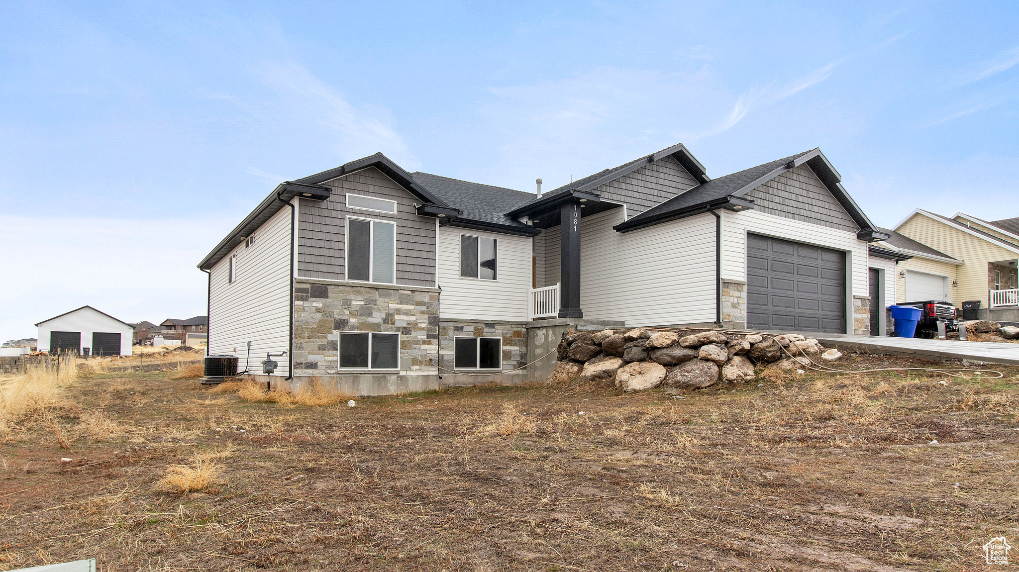 View of front of home with driveway, an attached garage, stone siding, and central AC