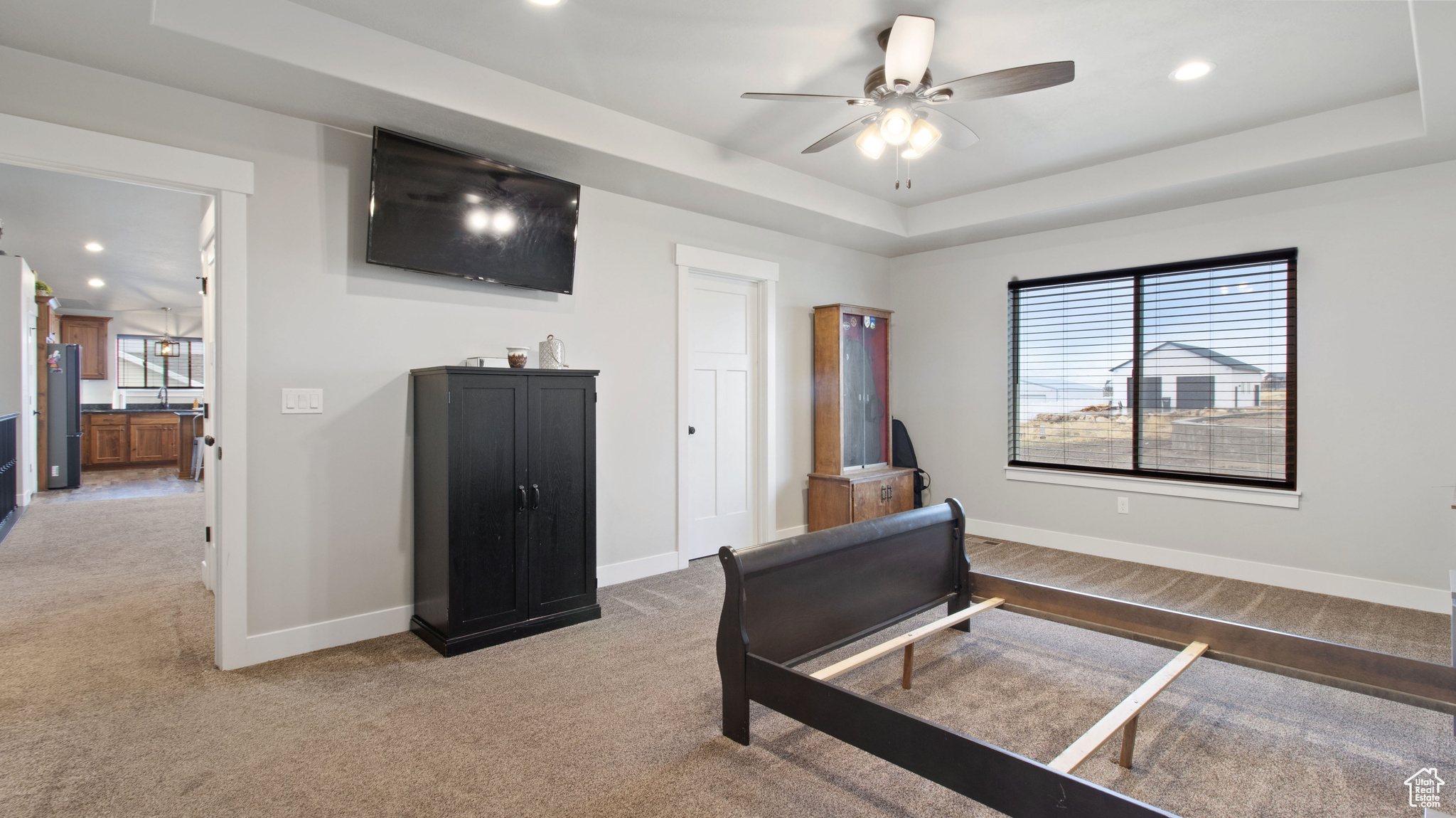 Bedroom featuring a raised ceiling, baseboards, freestanding refrigerator, and light carpet