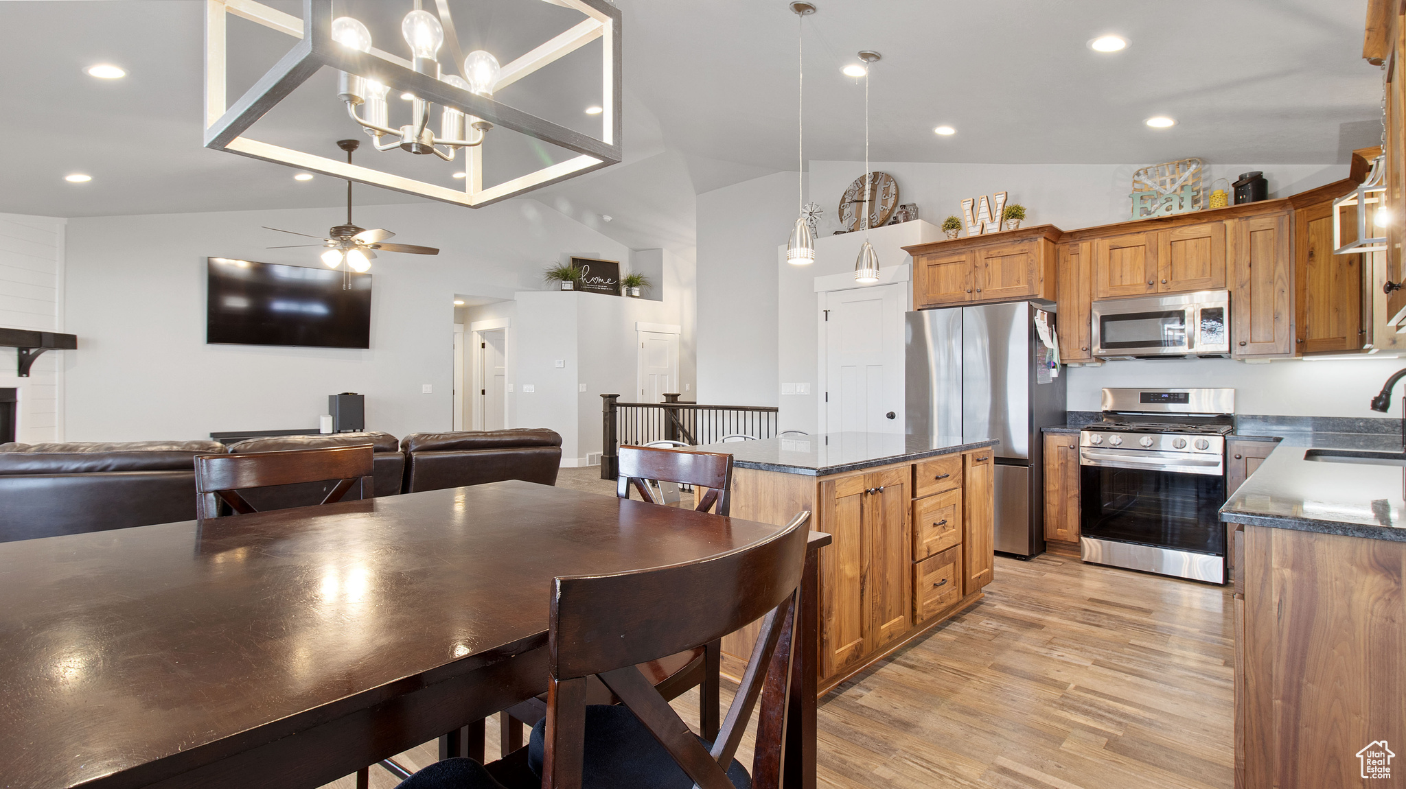 Kitchen with brown cabinets, light wood-style flooring, dark countertops, appliances with stainless steel finishes, and lofted ceiling