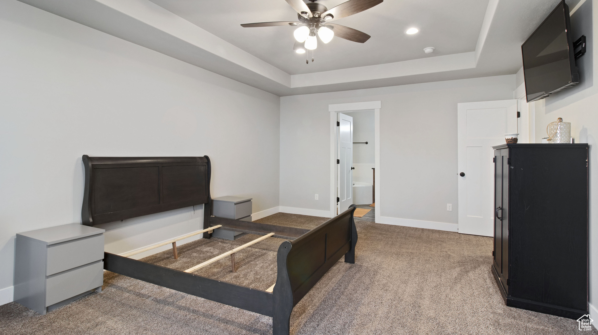 Bedroom with ceiling fan, baseboards, a tray ceiling, carpet floors, and ensuite bathroom