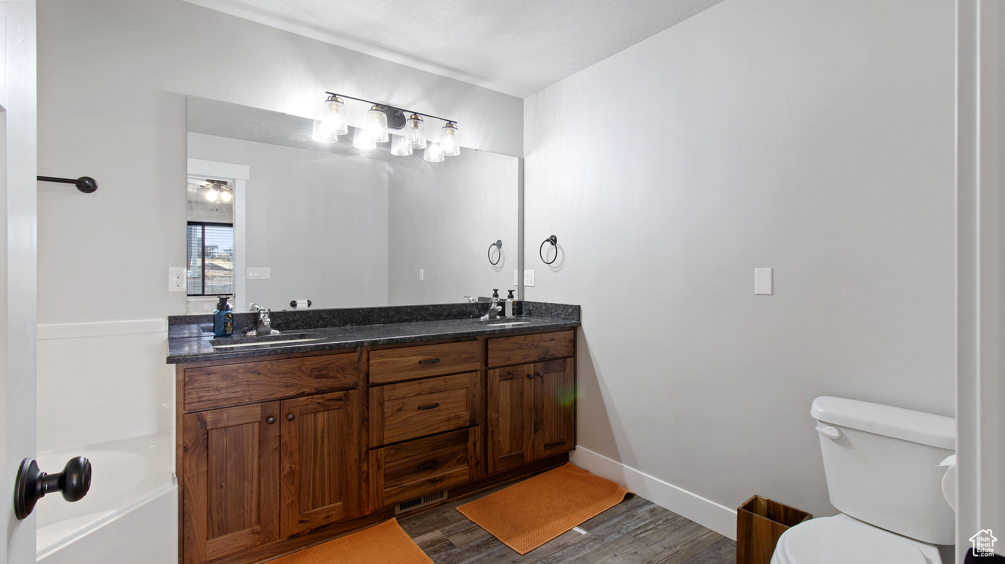 Full bathroom with wood finished floors, baseboards, double vanity, a sink, and toilet