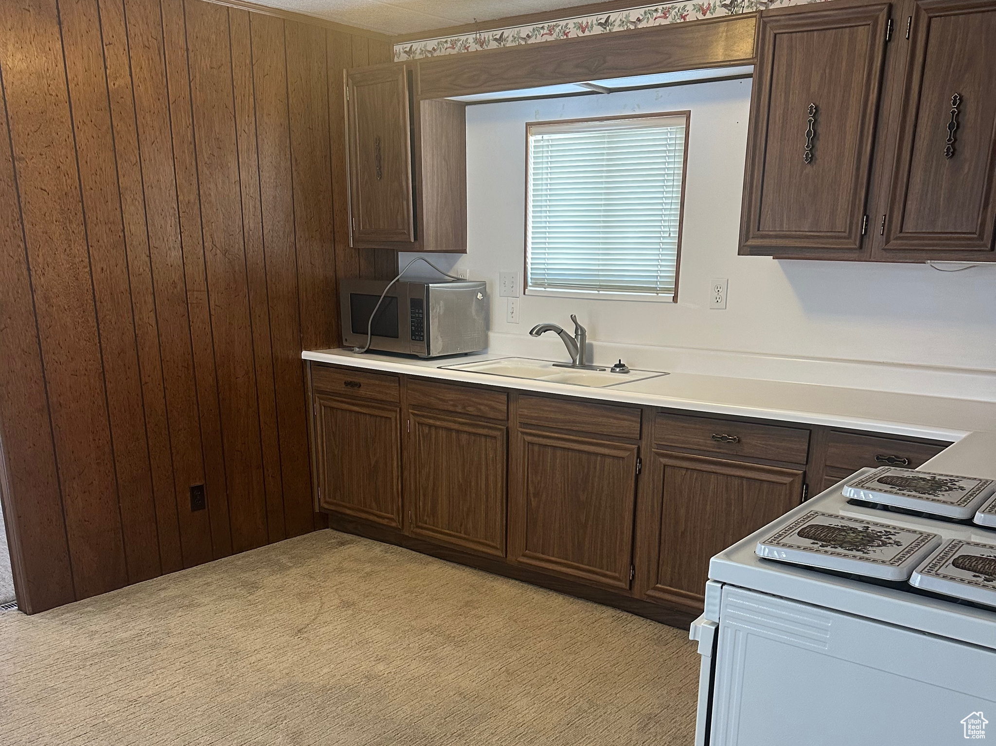 Kitchen featuring a sink, stainless steel microwave, range with electric stovetop, wood walls, and light countertops