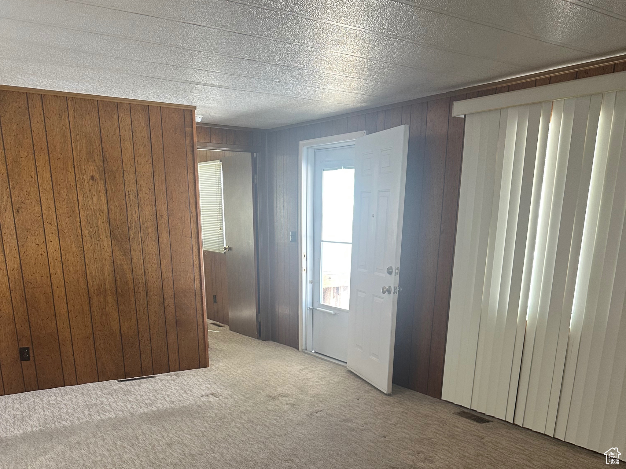 Unfurnished living room with visible vents, wood walls, a textured ceiling, and carpet floors