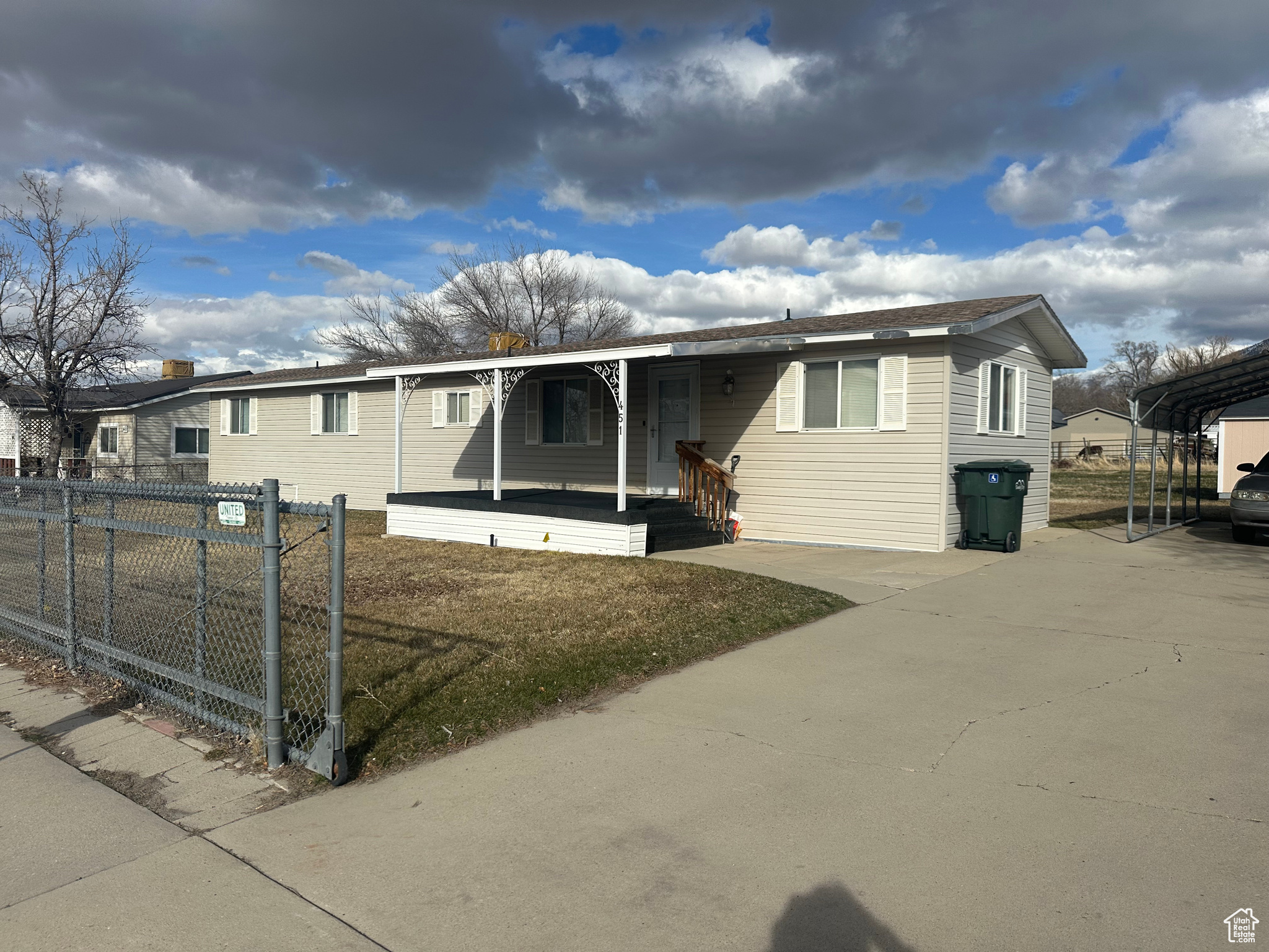 View of front of home featuring a carport, covered porch, concrete driveway, and fence