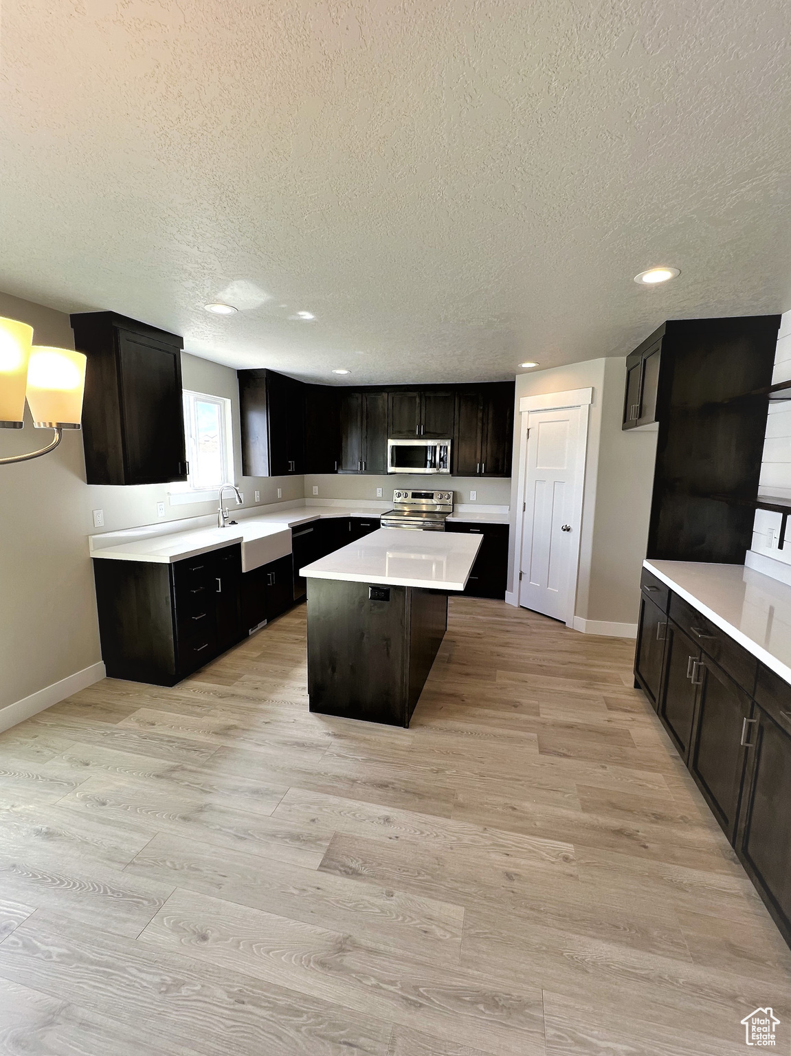 Kitchen with light countertops, light wood-type flooring, appliances with stainless steel finishes, and a center island
