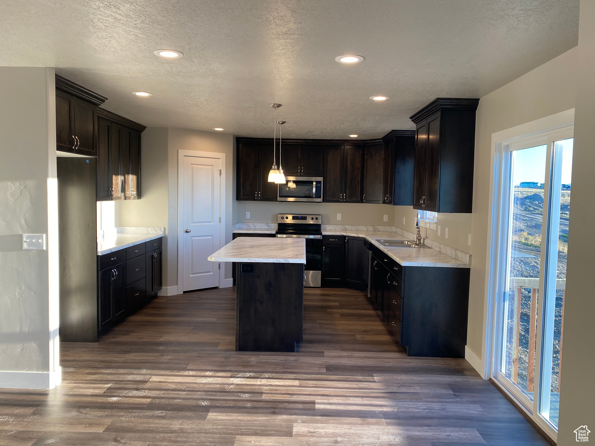 Kitchen with a sink, appliances with stainless steel finishes, dark wood-style flooring, and a center island
