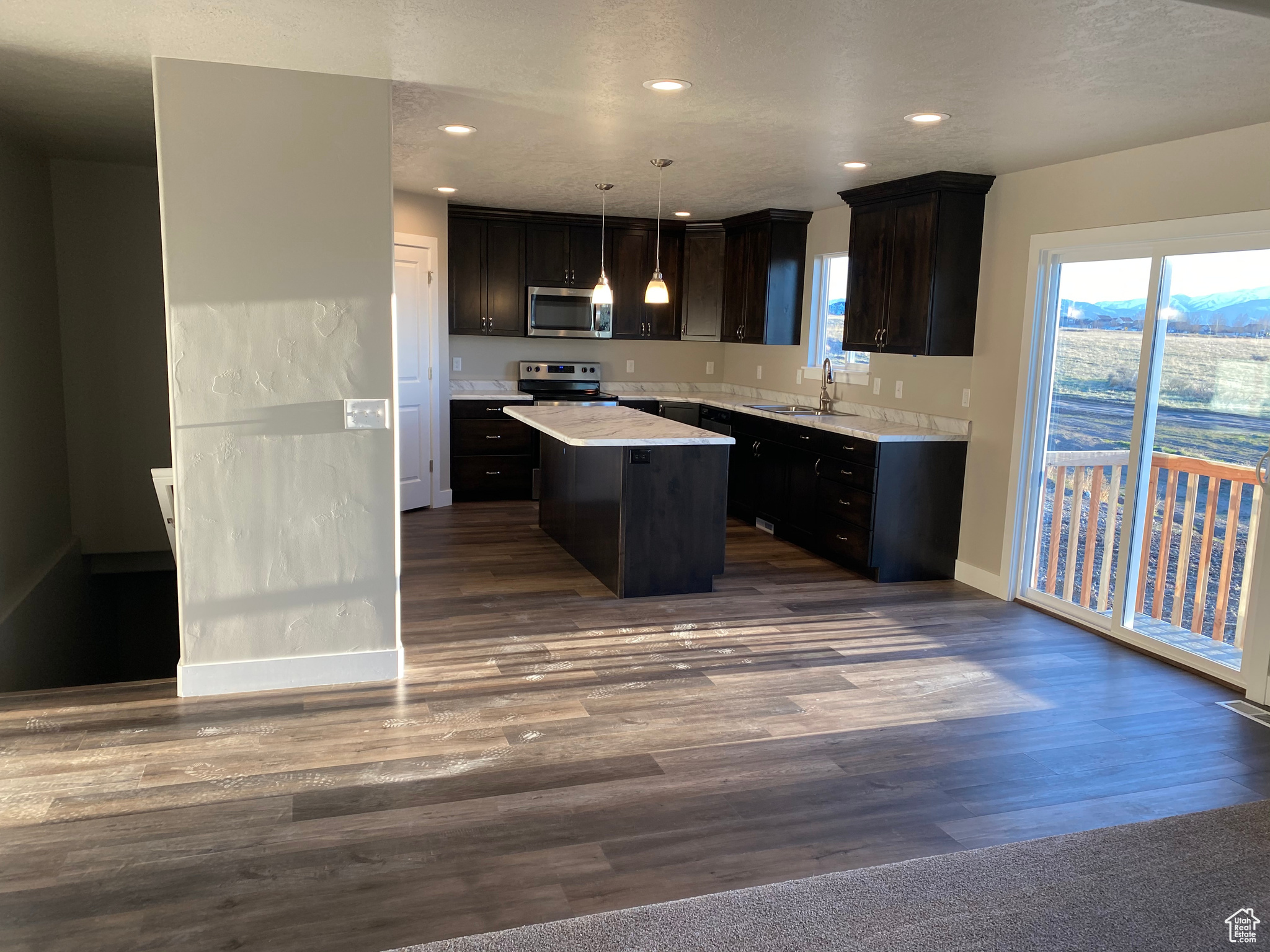 Kitchen with light countertops, dark wood-type flooring, appliances with stainless steel finishes, and a kitchen island