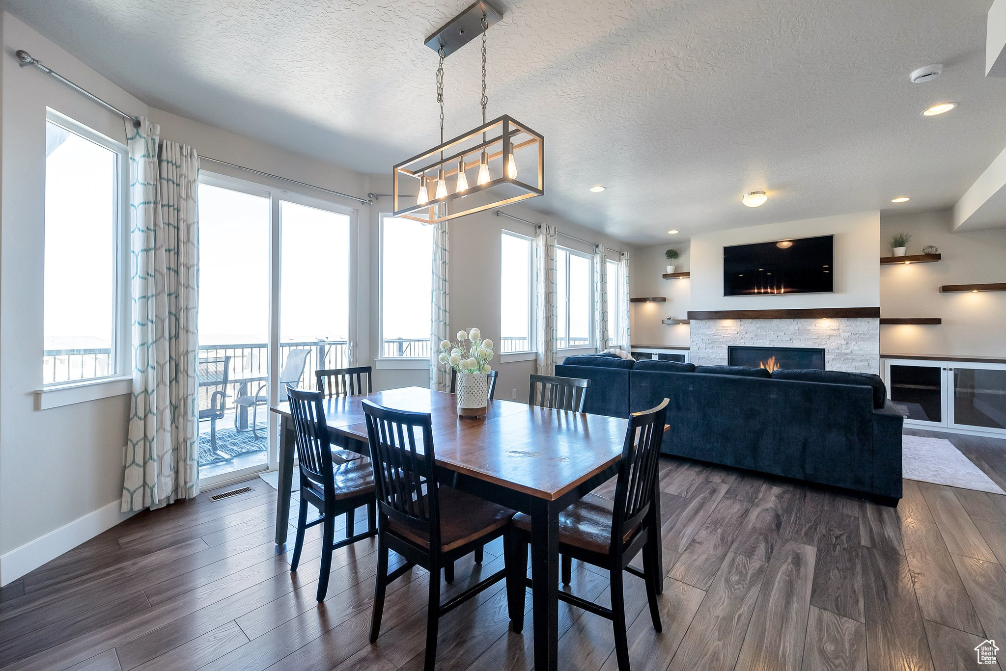 Dining space with visible vents, baseboards, dark wood finished floors, a lit fireplace, and a textured ceiling