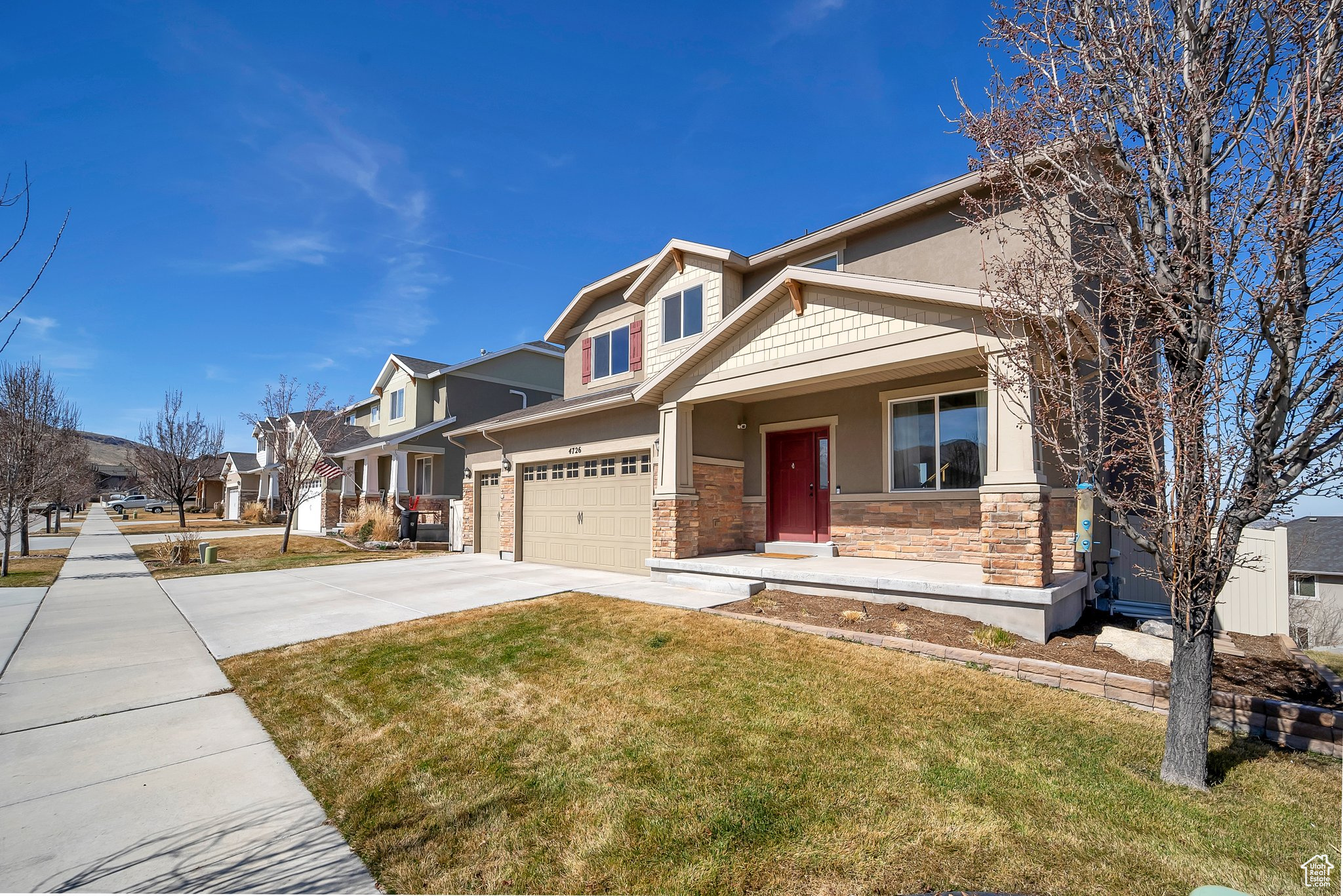 Craftsman-style house with stucco siding, stone siding, a residential view, concrete driveway, and a front yard