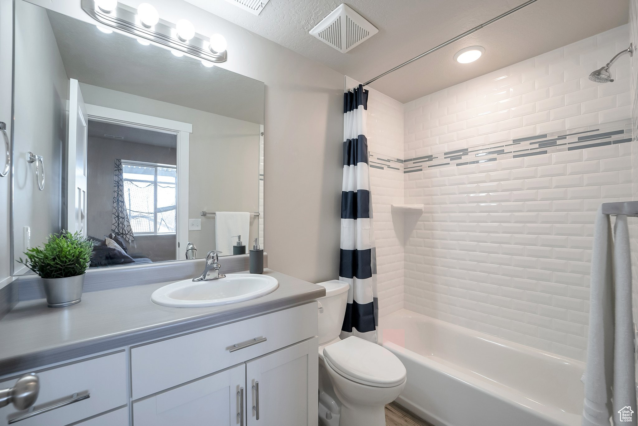 Bathroom featuring visible vents, toilet, vanity, and shower / bath combination with curtain