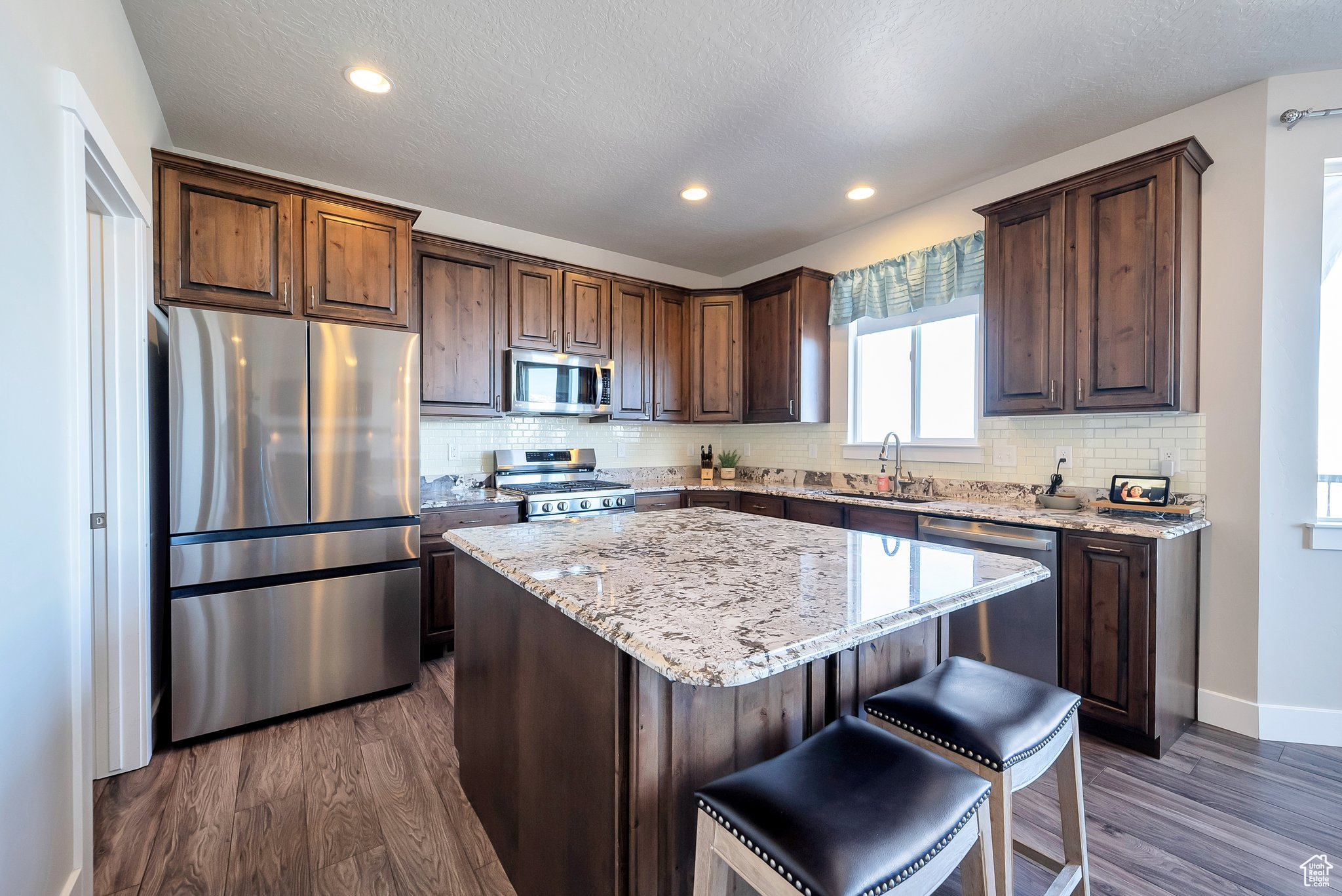 Kitchen featuring a center island, light stone countertops, stainless steel appliances, and dark wood-style flooring