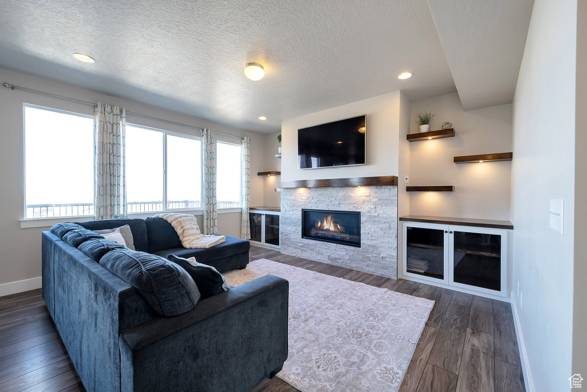 Living room featuring a textured ceiling, wood finished floors, recessed lighting, a stone fireplace, and baseboards