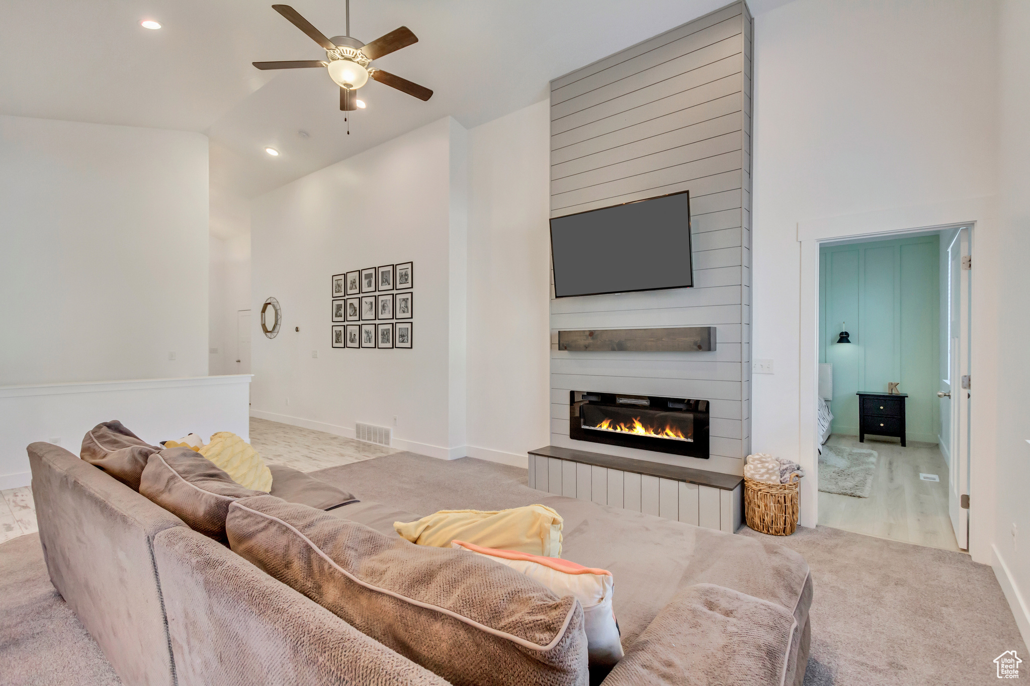 Carpeted living room with visible vents, baseboards, ceiling fan, a fireplace, and high vaulted ceiling