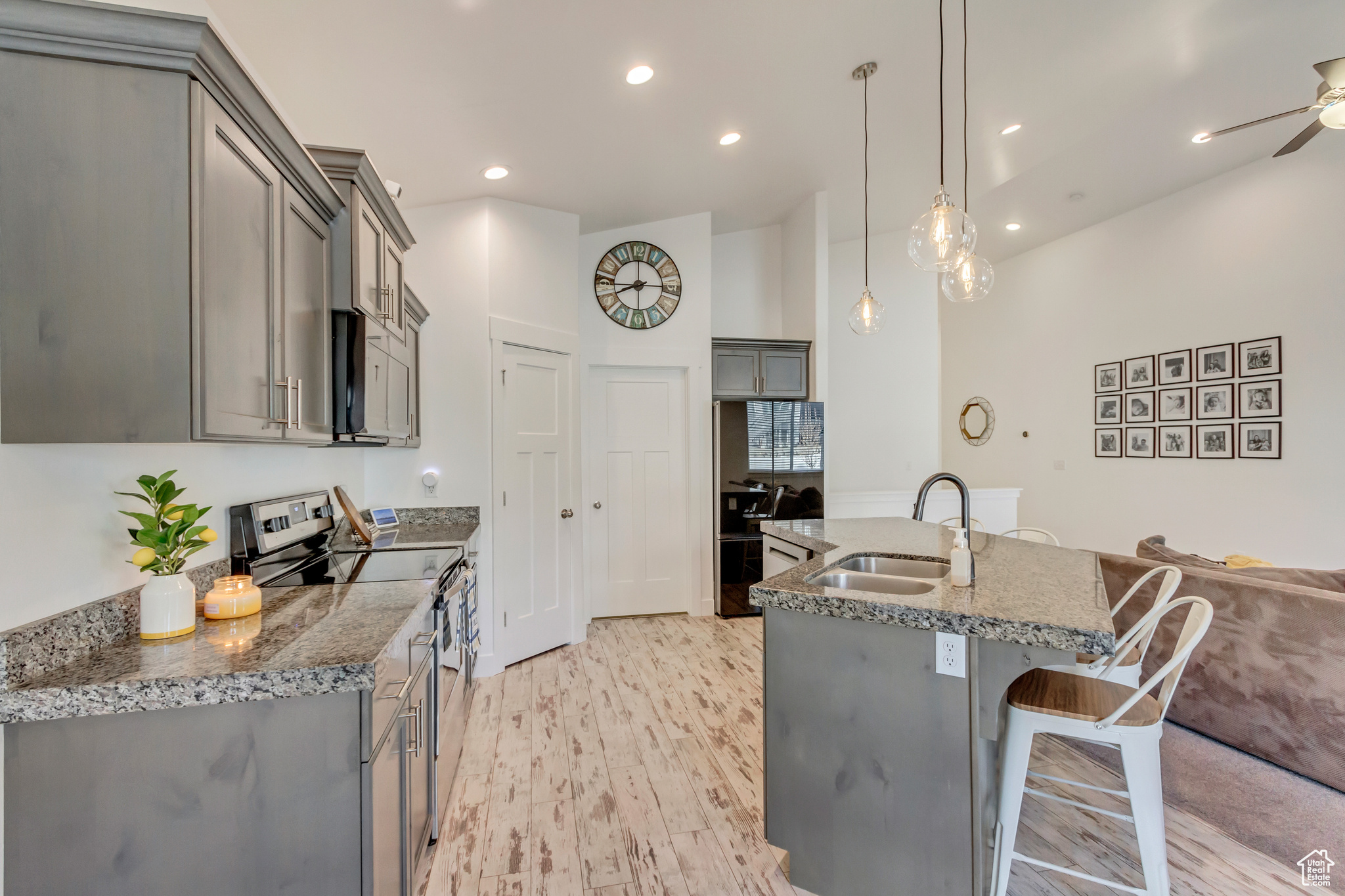 Kitchen with stainless steel electric range oven, stone countertops, gray cabinetry, a sink, and a kitchen bar