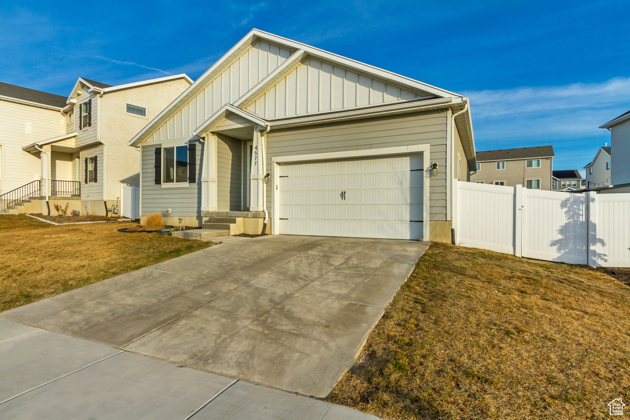 View of front facade featuring board and batten siding, fence, concrete driveway, a front yard, and an attached garage