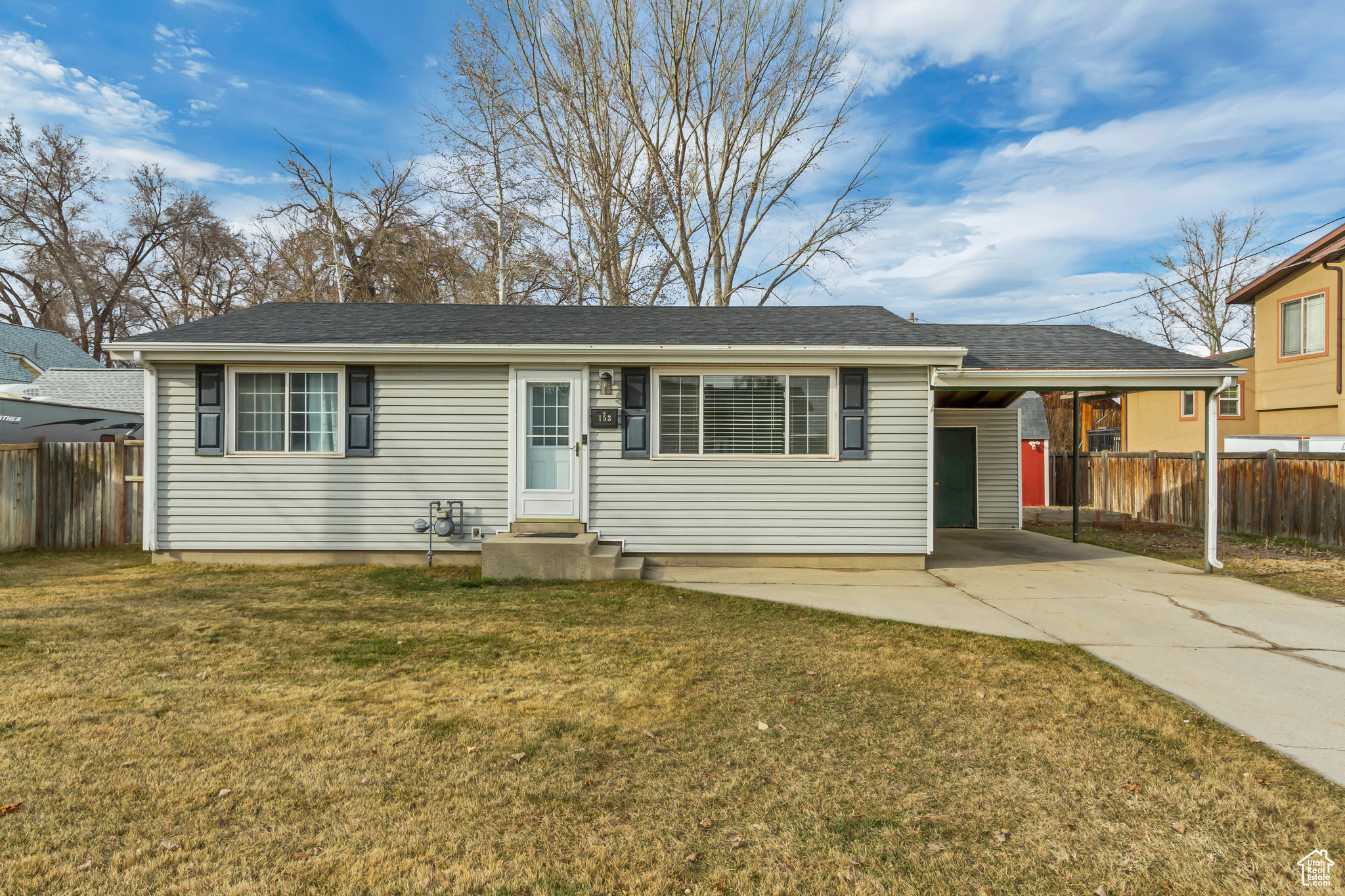 Ranch-style house featuring a front lawn, driveway, entry steps, fence, and a carport