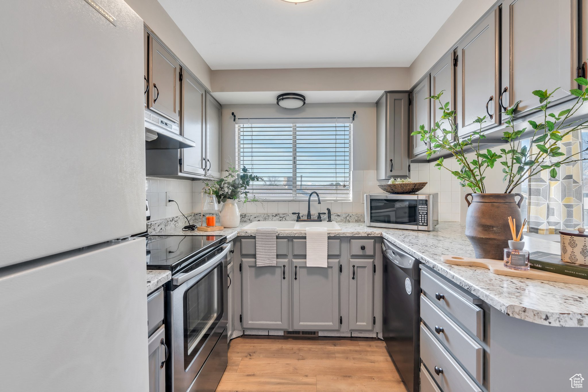 Kitchen with gray cabinetry, light wood-style flooring, backsplash, stainless steel appliances, and extractor fan