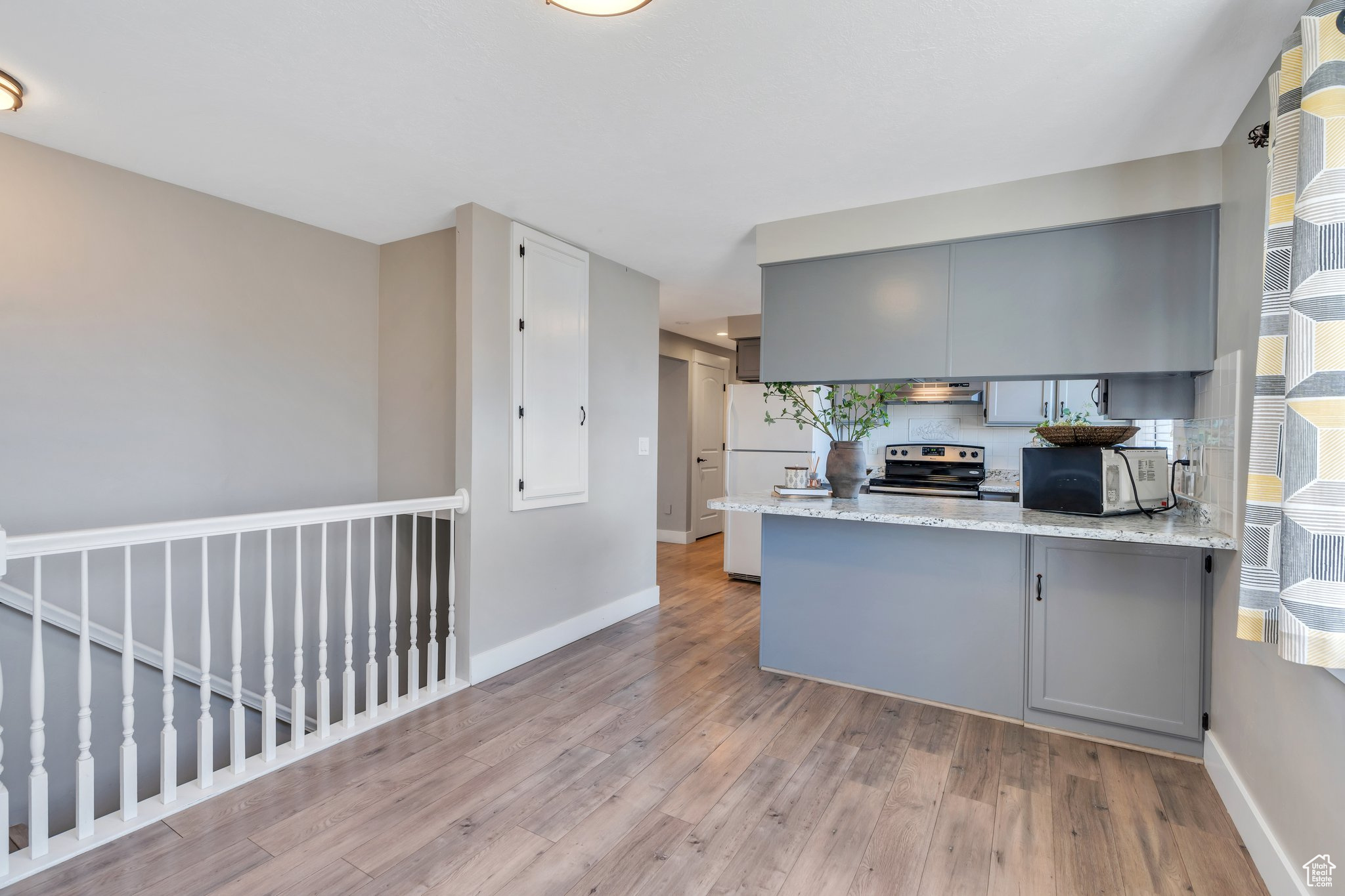 Kitchen featuring baseboards, a peninsula, gray cabinets, stainless steel range with electric cooktop, and light wood-style floors