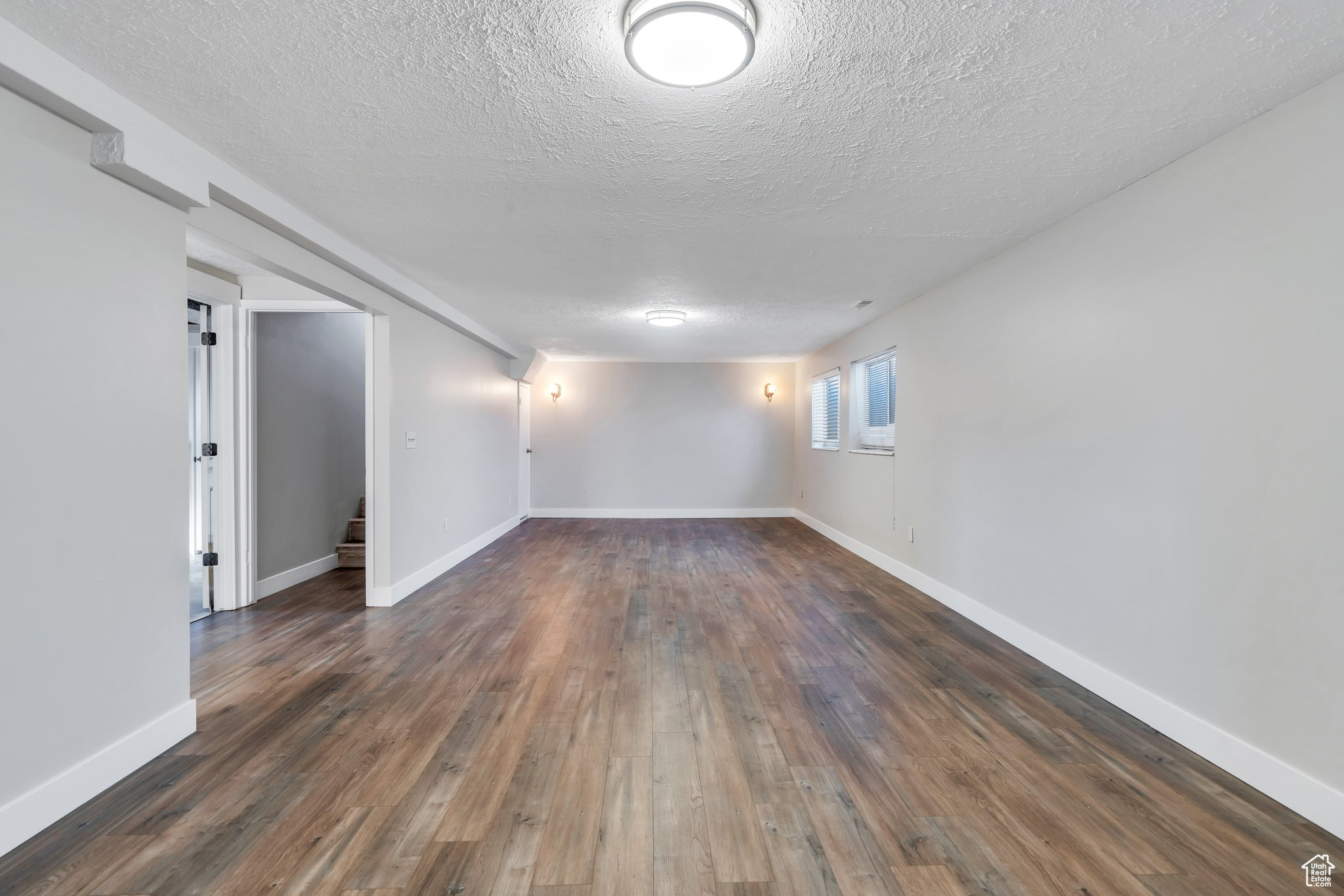 Unfurnished room with stairway, a textured ceiling, baseboards, and hardwood / wood-style flooring