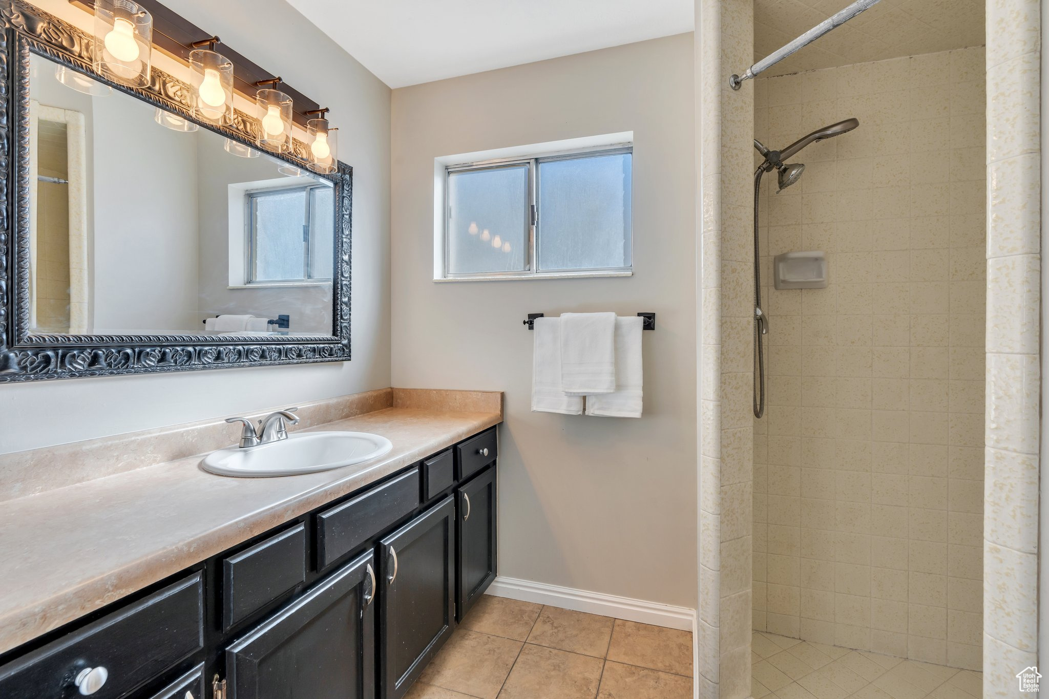 Bathroom with a tile shower, tile patterned floors, vanity, and baseboards