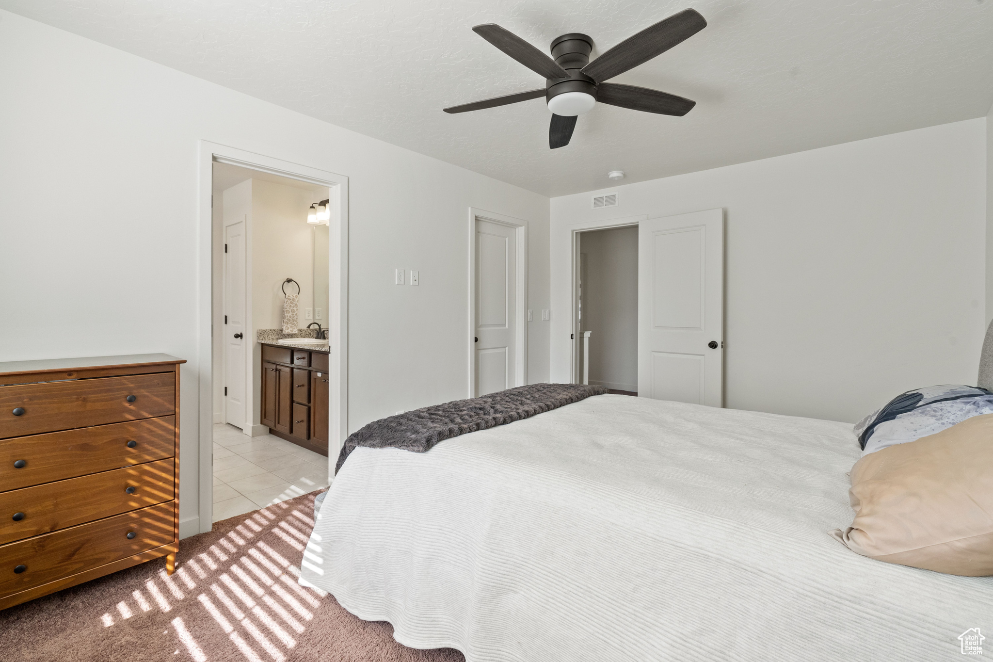 Bedroom with visible vents, ensuite bathroom, a sink, light tile patterned floors, and light colored carpet