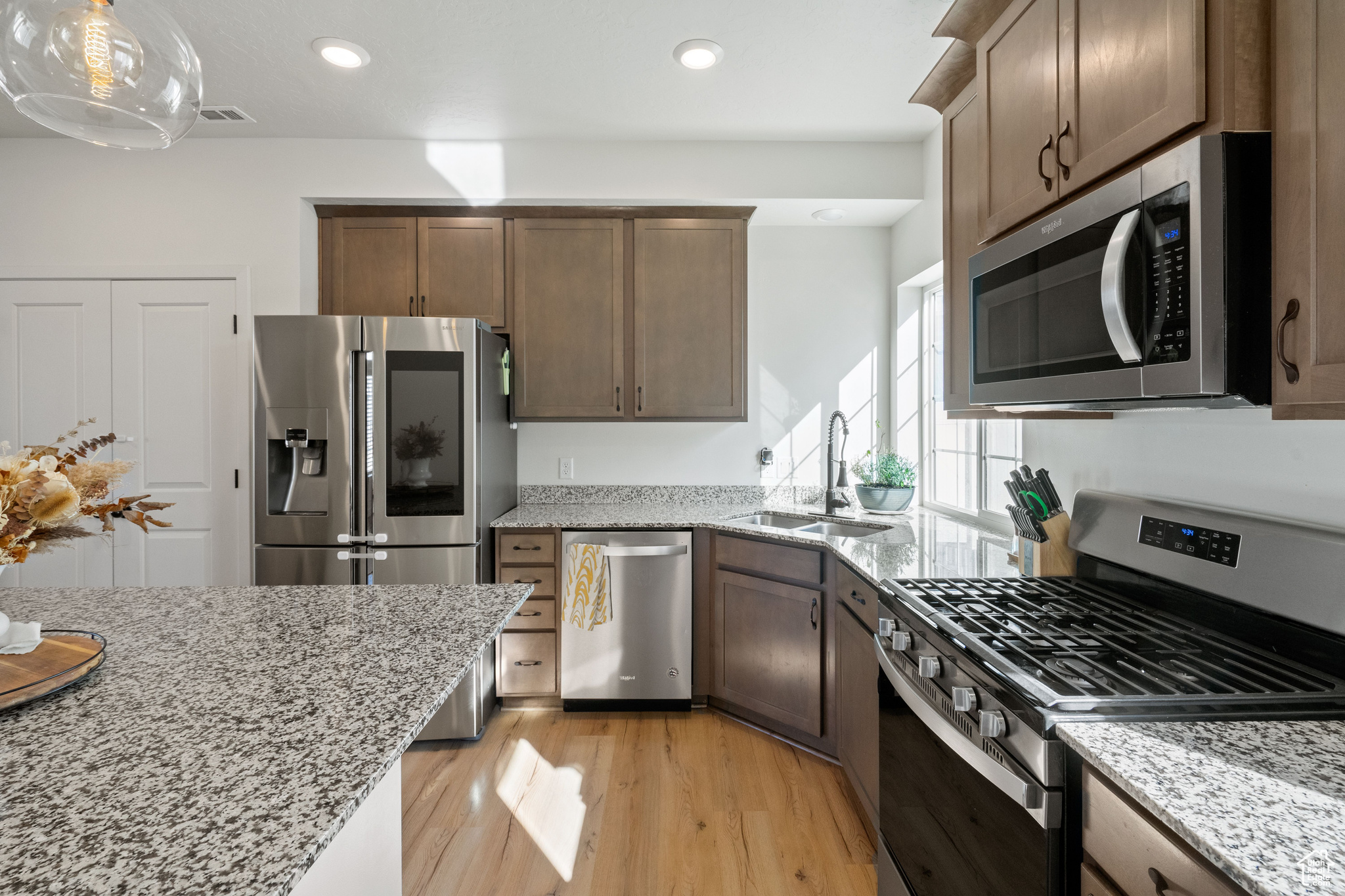 Kitchen featuring visible vents, light wood-style flooring, a sink, light stone counters, and appliances with stainless steel finishes